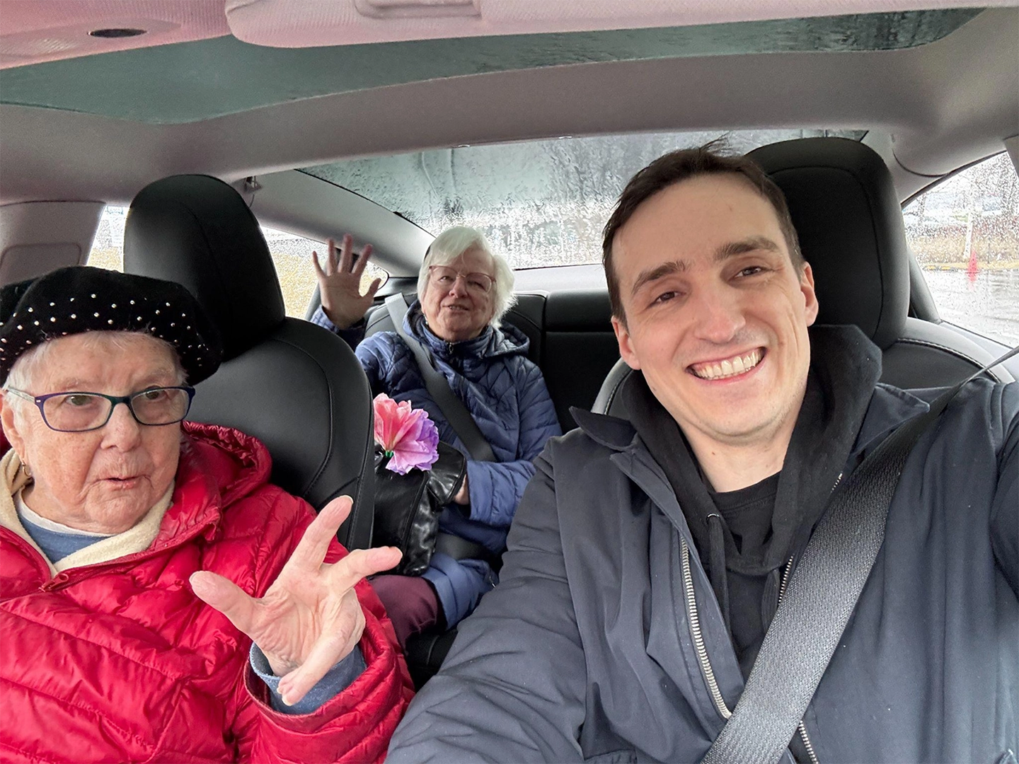 Tony Aubé in a car with seniors, smiling during a Petits Frères outing.